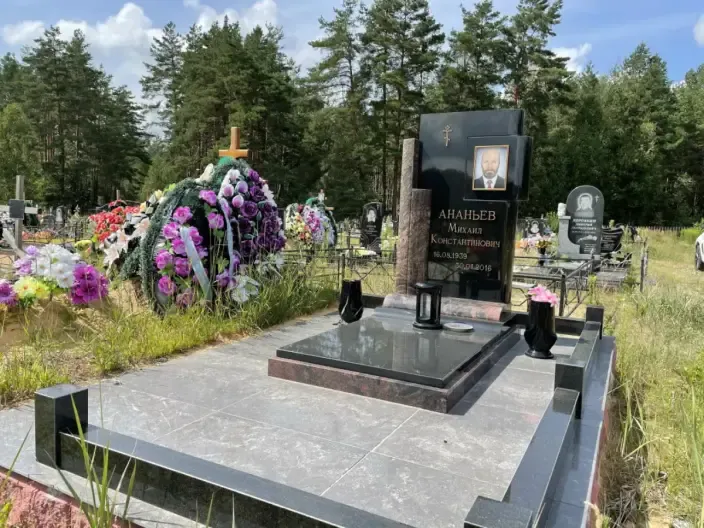 Памятник прямоугольной формы из чёрного гранита с металлической оградой и цветником